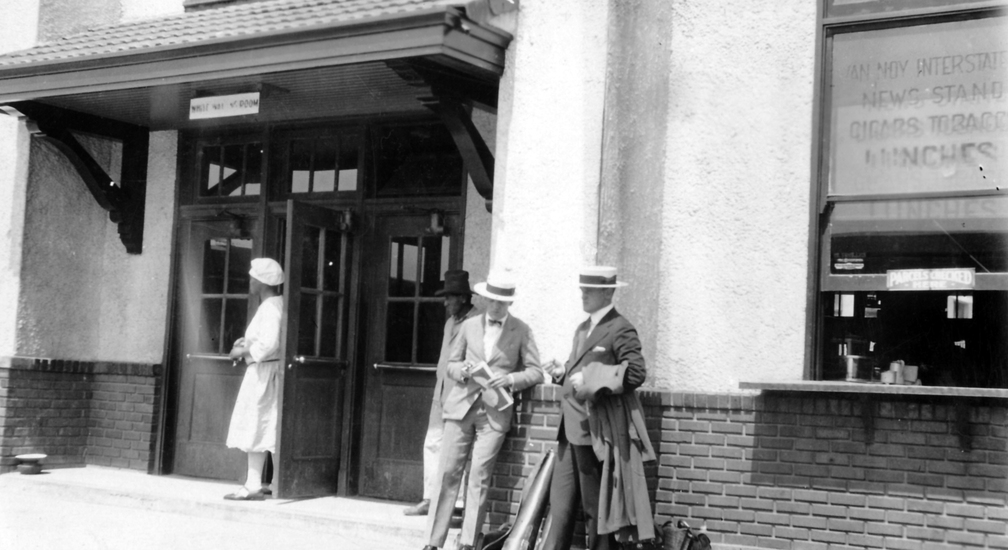 Bahnhofaufenthalt. Ein Kiosk der Van NOY Kette bietet Zeitungen, Rauchwahren und Mittagessen. An Bord der Züge gab es damals noch keine Speisewagen.